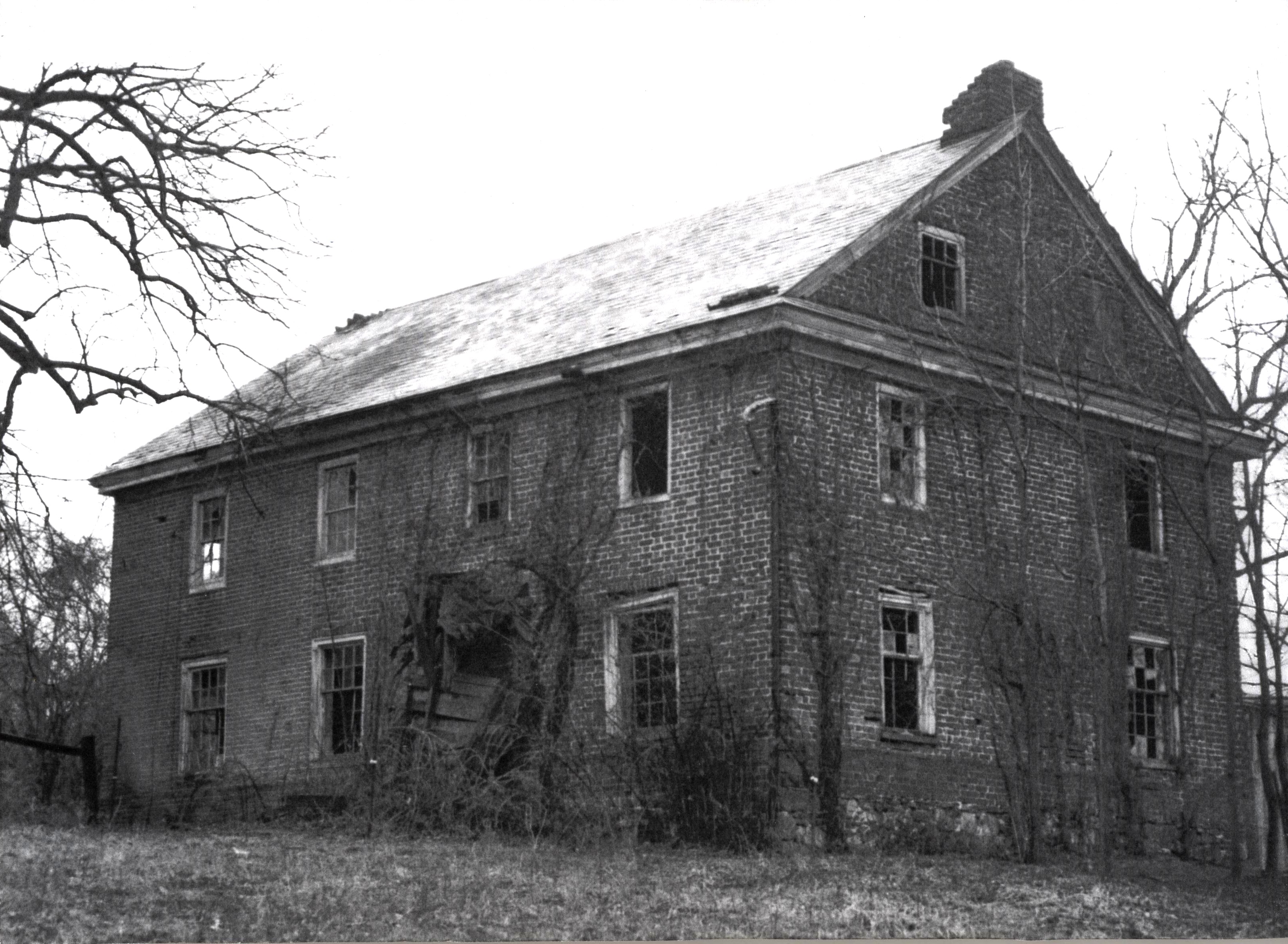An old home with broken windows, a collapsed entryway, and visible damage to the roof, walls and chimney.